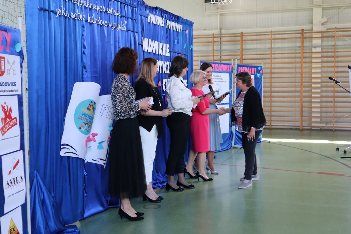 Dyrektor ZSP, kierownnik Biblioteki i przedstawiciel z urządu Gminy Spytkowice wręczają uczestnikom konkursu dyplomy i nagrody. Obok dwie kobiety, które podają prowadzącym nagrody i dyplomy.
